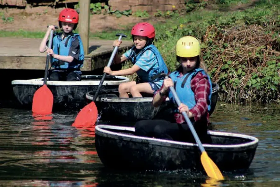 Young people paddling coracles on the pool