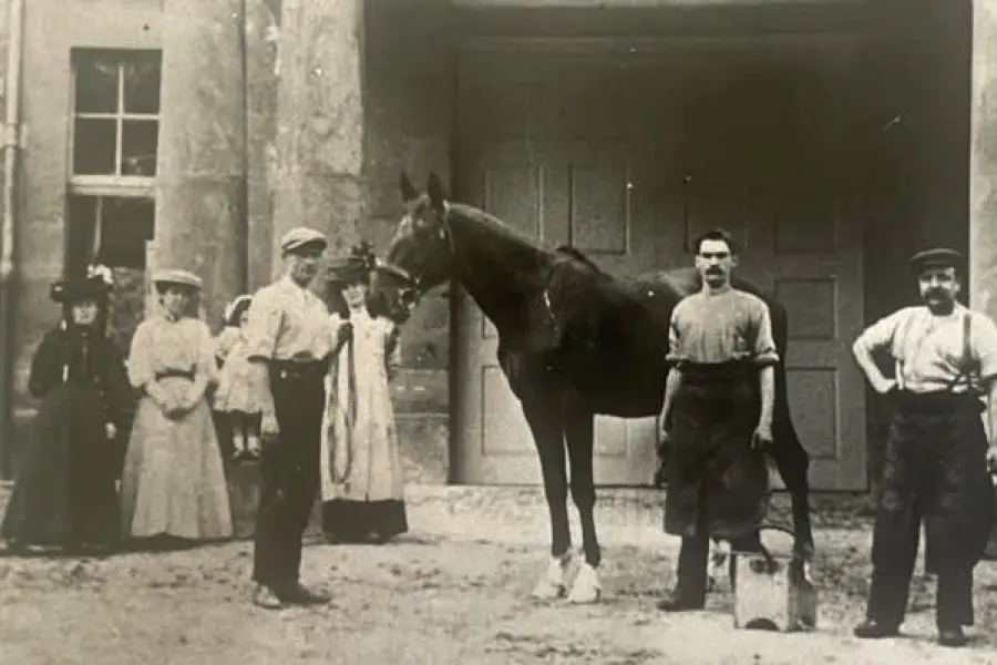 Coach house and stable staff with a horse, around 1900